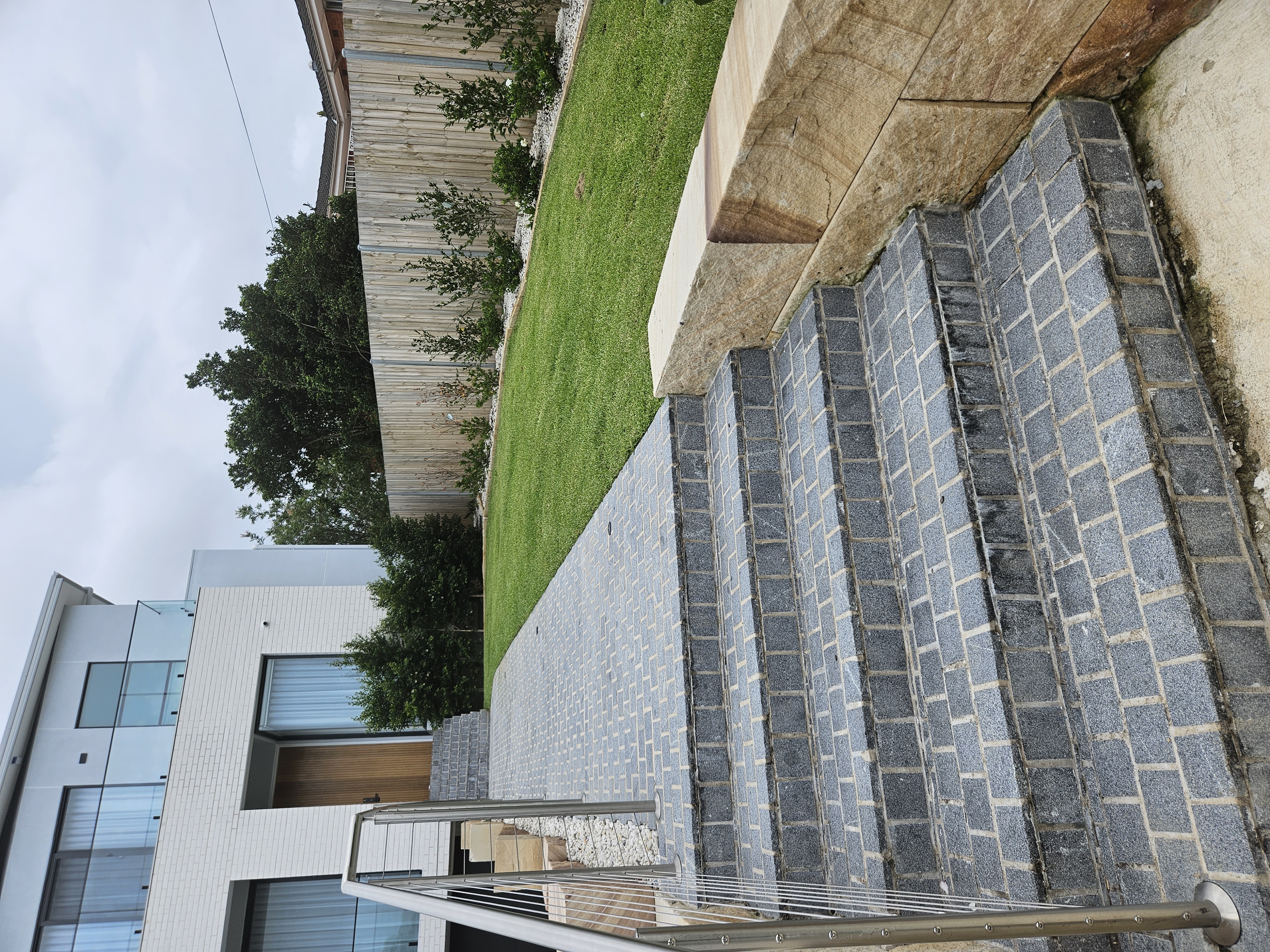 Sandstone block retaining wall beside bluestone cobble steps and lawn at a Sydney home